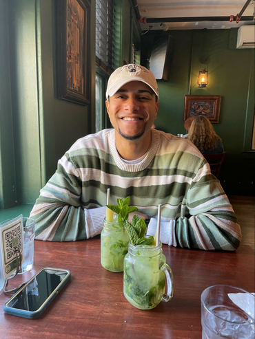 Joe White, a young man with a beard, smiles at the camera. He's wearing a green-striped shirt and a ball cap.